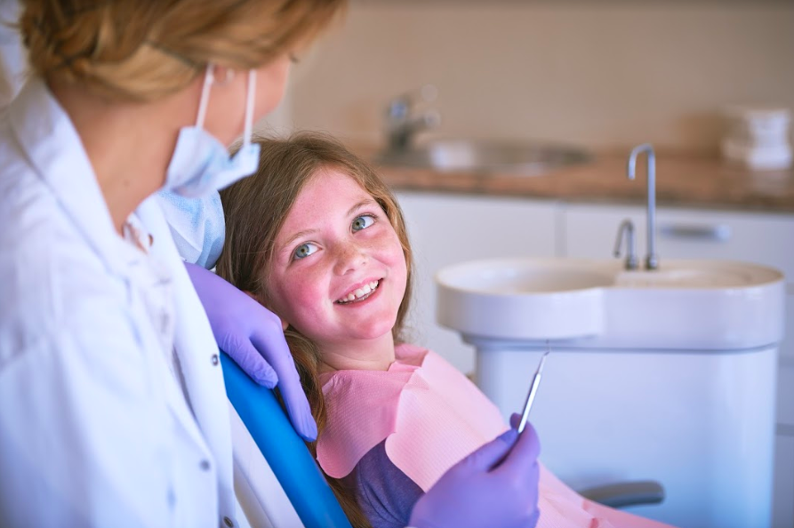 young girl in dentist chair looking at dentist